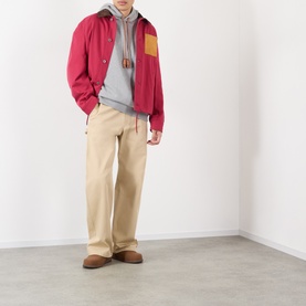 Model wearing Loewe grey melange cotton hoodie, styled with red zip jacket, beige trousers and brown suede loafers.