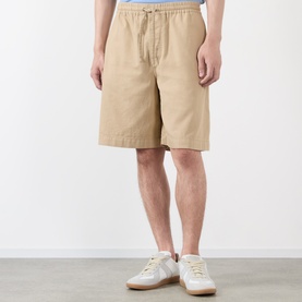 Model wearing Loewe beige cotton shorts with elasticated drawstring waist, styled with white low-top trainers.