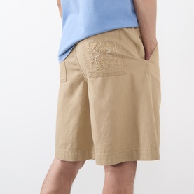 Model wearing Loewe beige cotton shorts with tonal embroidered detail on rear pocket, styled with a light blue top.
