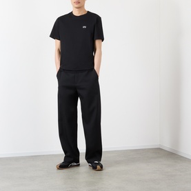 Model wearing Loewe black cotton T-shirt with small chest logo, styled with wide-leg black trousers and black sandals.