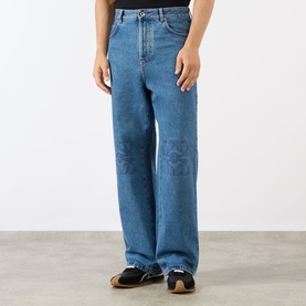 Model wearing Loewe Anagram Logo Baggy Jeans in jeans blue, mid-wash denim with tonal Anagram logo detailing at the knees, styled with sandals.