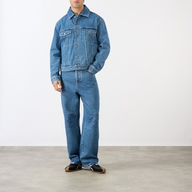 Model wearing Loewe Anagram Logo Baggy Jeans in jeans blue, mid-wash straight-leg denim styled with a matching denim jacket and brown shoes.
