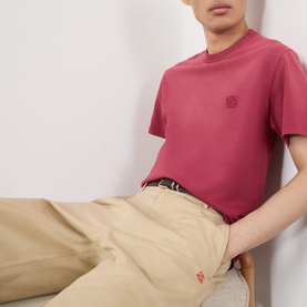 Model wearing Loewe red cotton T-shirt with tonal Anagram logo, styled with beige trousers and black belt.