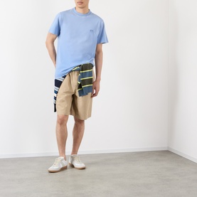 Model wearing Loewe Tonal Anagram Logo T-Shirt in blue, styled with beige shorts and a striped jacket tied at the waist.