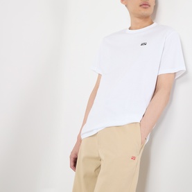 Model wearing Loewe white cotton T-shirt with small chest logo patch, styled with beige trousers featuring red logo detail.