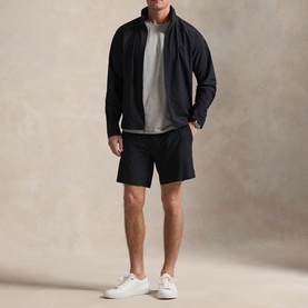 Model wearing RLX Golf black casual jacket with zip fastening, styled with grey sweatshirt, black shorts and white trainers