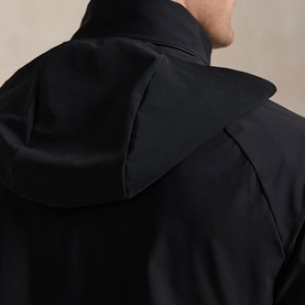 Model wearing RLX Golf black casual jacket, rear close-up showing structured hood and cape-style back panel detail.