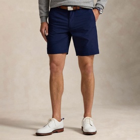 Model wearing RLX Golf shorts in Refined Navy with brown belt, styled with white leather lace-up shoes and grey sweatshirt.