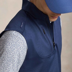 Model wearing RLX Golf Logo Quarter-Zip Gilet in Spring Navy Heather, styled with a printed long-sleeve top and navy cap.