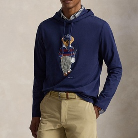 Model wearing RLX Golf Refined Navy long-sleeve hooded tee with Polo Bear golf graphic, styled with khaki trousers and striped shirt underneath.