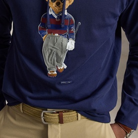 Model wearing RLX Golf T-Shirt in Refined Navy, featuring a golf bear graphic print, styled with beige trousers and a striped belt.