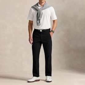 Model wearing RLX Golf trousers in Polo Black, styled with a white polo shirt, grey scarf, and white leather shoes.