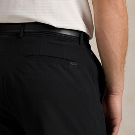 Model wearing RLX Golf trousers in Polo Black, close-up of rear view showing black belt and logo tab detail, styled with white shirt