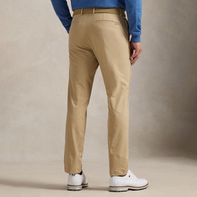 Model wearing RLX Golf beige trousers, rear view, styled with a blue knit and white golf shoes.