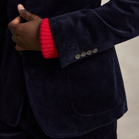 Model wearing navy blue corduroy blazer with four-button cuff detail, styled with a red ribbed knit jumper underneath
