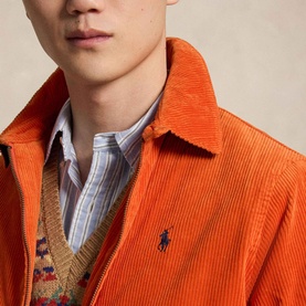 Model wearing Ralph Lauren College Orange corduroy casual jacket with navy Polo logo, styled over a striped shirt and knit vest.