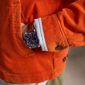 Model wearing Ralph Lauren College Orange corduroy casual jacket, styled with a white shirt and brown-strapped watch at wrist.