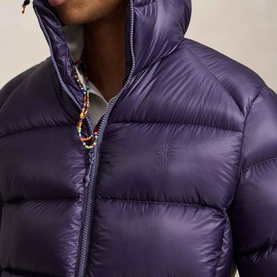 Model wearing Ralph Lauren junberry quilted puffer jacket with hood, styled with a multicoloured beaded necklace.