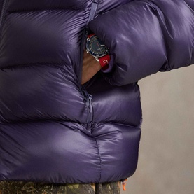 Model wearing Ralph Lauren junberry quilted down jacket, close-up of hand pocket detail with red watch and camouflage trousers visible.