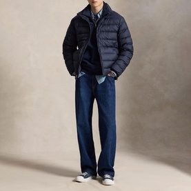 Model wearing navy puffer jacket, styled with navy knitwear, light blue shirt, dark indigo jeans, and white canvas trainers
