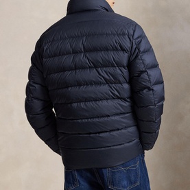 Model wearing navy quilted puffer jacket, rear view, with ribbed hem and cuffs, styled with light blue jeans
