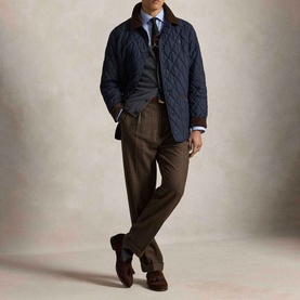 Model wearing Ralph Lauren navy quilted casual jacket, styled with grey knitwear, blue shirt, brown trousers and dark suede loafers.