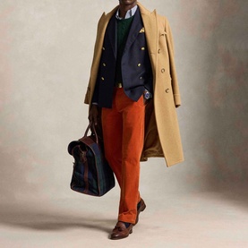 Model wearing Ralph Lauren Pony Logo Straight Leg Corduroy Trousers in Charles Orange, styled with camel coat, navy blazer, and brown loafers.