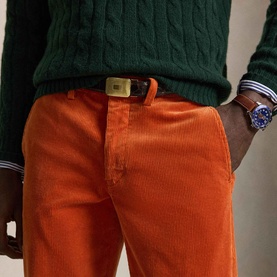 Model wearing Ralph Lauren Pony Logo Straight Leg Corduroy Trousers in Charles Orange, styled with green cable-knit sweater and leather belt.