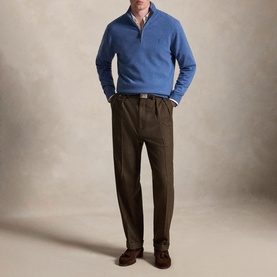 Model wearing blue quarter-zip knit jumper with shirt collar visible, styled with olive pleated trousers and dark brown shoes