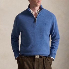 Model wearing blue half-zip knit sweater with embroidered logo, styled with white collared shirt and brown tweed trousers