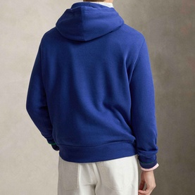 Model wearing Ralph Lauren The RL Pony Logo Fleece Hoodie in Blue Yacht, back view, styled with white trousers.