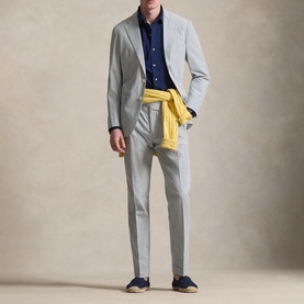 Model wearing light grey suit with navy shirt, yellow knitwear tied at waist, and navy loafers