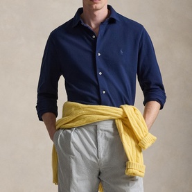 Model wearing navy Polo Ralph Lauren button-up shirt with chest logo, styled with grey trousers and yellow knitwear tied at waist