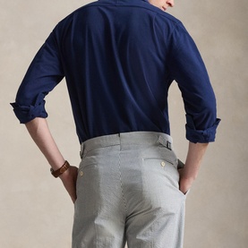 Model wearing navy blue long-sleeve shirt with rolled cuffs, styled with light grey trousers, viewed from behind