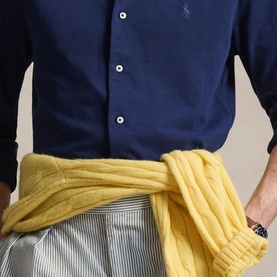 Model wearing navy button-down shirt with yellow knit sweater tied at waist, styled with grey striped trousers