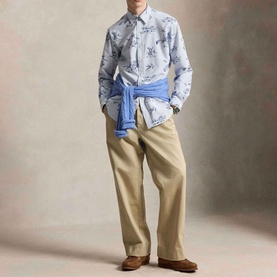 Model wearing Ralph Lauren Dog & Pheasant Logo Striped Oxford Shirt in blue scenic print, styled with beige trousers and a blue jumper tied at the