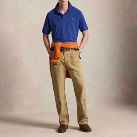 Model wearing Ralph Lauren Pony Logo Slim Fit Mesh Polo in Blue Yacht, styled with khaki trousers and orange jumper tied at waist.