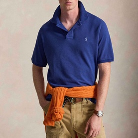 Model wearing Ralph Lauren Pony Logo Slim Fit Mesh Polo Shirt in Blue Yacht, styled with khaki trousers and orange jumper tied at waist.