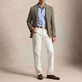 Model wearing Ralph Lauren Pony Logo Slim Fit Oxford Shirt in chambray blue, styled with grey blazer, white trousers, and brown loafers.