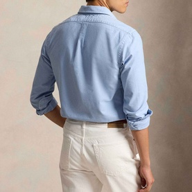 Model wearing Ralph Lauren Pony Logo Slim Fit Oxford Shirt in Chambray Blue, back view, styled with white trousers and brown belt.