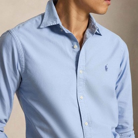 Model wearing Ralph Lauren Pony Logo Slim Fit Oxford Shirt in chambray blue, featuring embroidered pony logo and button placket.