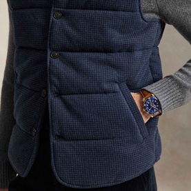 Model wearing Ralph Lauren navy dogtooth gilet with front pockets, styled with grey knitwear and a blue and rose gold watch.