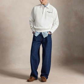 Model wearing Ralph Lauren white sweatshirt with quarter zip, styled with light blue shirt, dark indigo wide-leg jeans and brown loafers