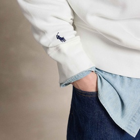 Model wearing Ralph Lauren white sweatshirt with embroidered Polo Pony logo, styled with light blue shirt and dark indigo jeans.