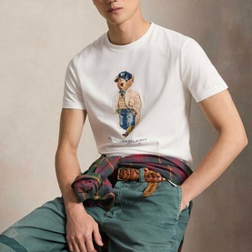 Model wearing Ralph Lauren Polo Bear Custom Slim Fit T-Shirt in white with crew neck and Polo Bear graphic print, styled with green trousers.