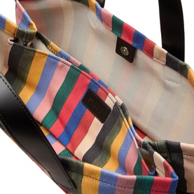 Staud Port Stripe Tote Bag interior showing multicolour Artist Stripe lining, inner pocket, logo badge, and black leather trim with magnetic snap