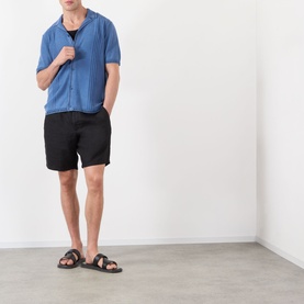 Model wearing Wax London Ivy Washed Shirt in blue, camp collar, short sleeves, styled with black shorts and dark sandals