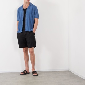 Model wearing Wax London Ivy Washed Shirt in blue with camp collar and short sleeves, styled with black shorts and sandals.