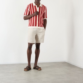 Model wearing Wax London Porto Striped Cardigan in ecru and orange, styled with cream shorts and brown leather sandals.