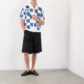 Model wearing Wax London Porto Printed Cardigan in ecru and blue check knit, styled with black shorts and loafers.